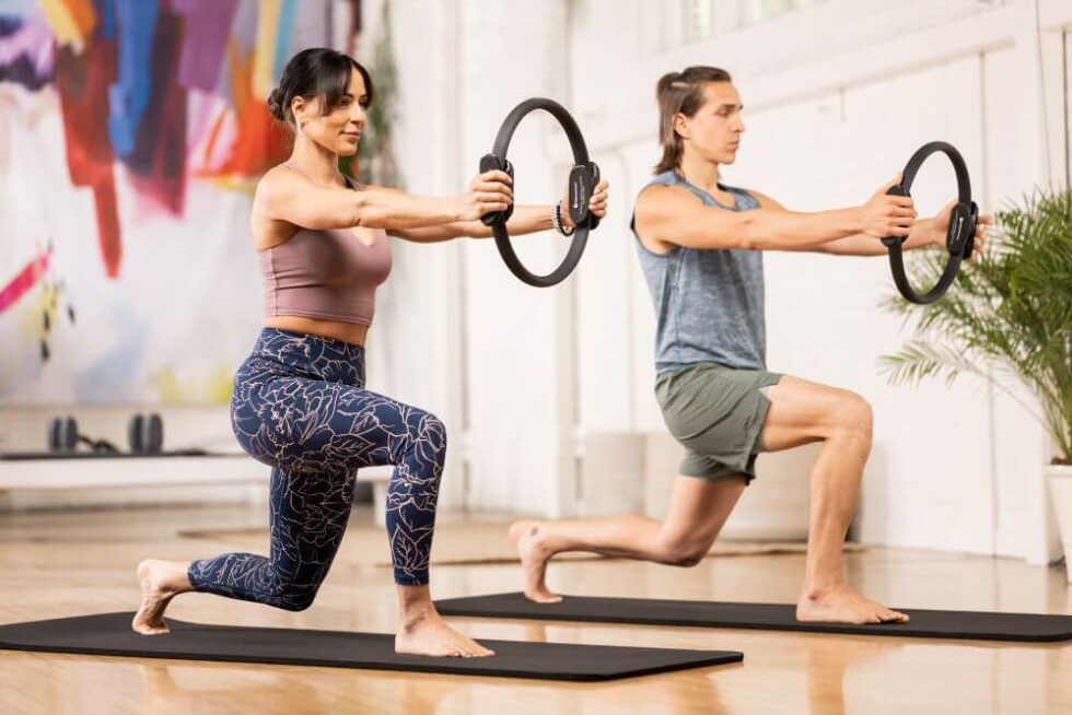 Du žmonės atlieka įtūpstus su Ultra-Fit ratu studijoje.