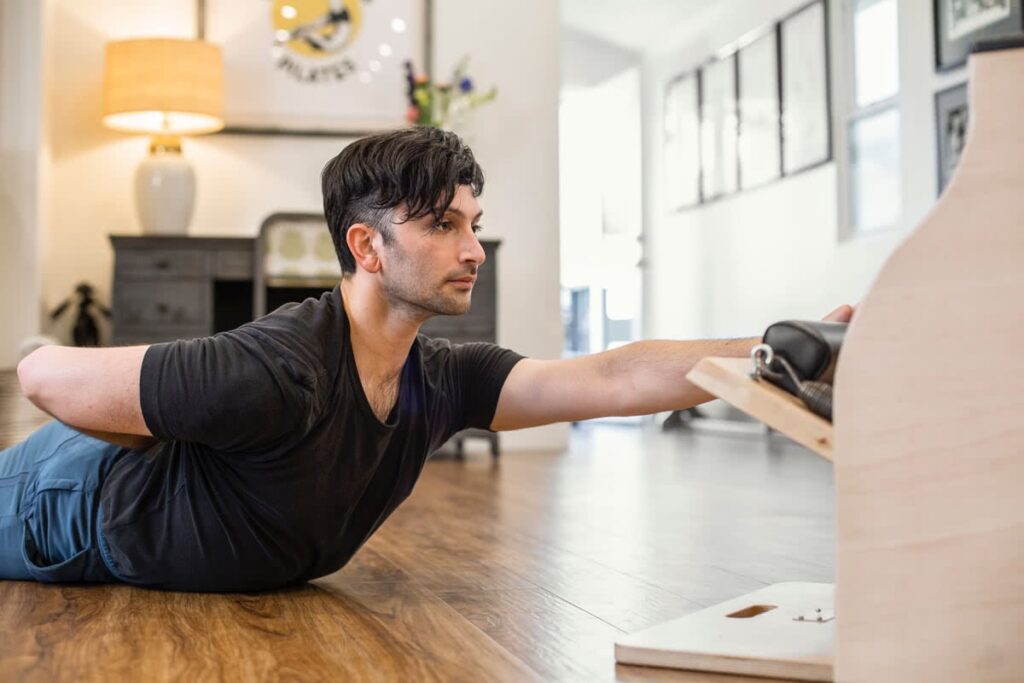 Man exercises on Contrology Wunda Chair, performing stretch.