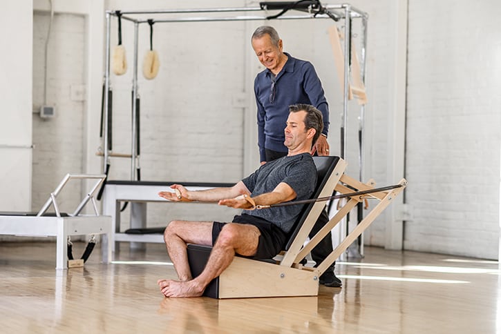 Vyras sportuoja su Contrology rankų kėde Pilates studijoje.