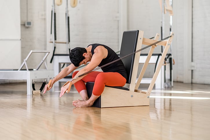 Instruktorius demonstruoja pratimą su Contrology rankų kėde studijoje.