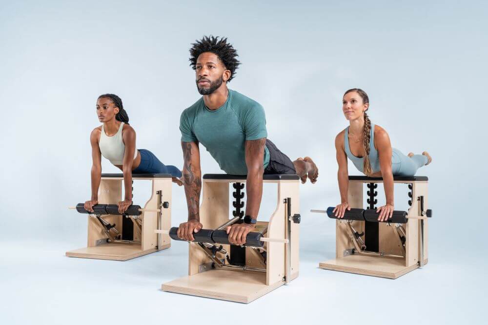 Three people exercising on Balanced Body Combo Chairs in a studio.