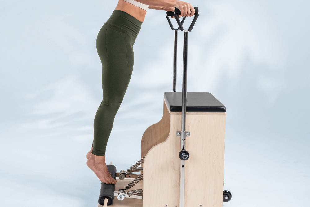Pilates Combo Chair with user standing and gripping handles.