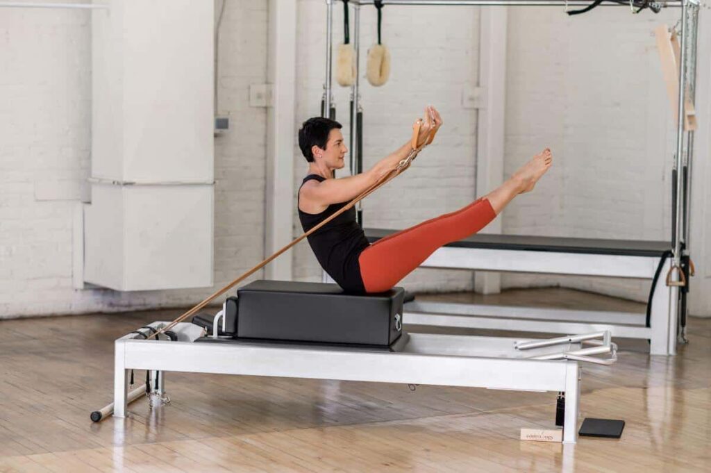 Человек выполняет сидячее упражнение Пилатеса на боксе Contrology.