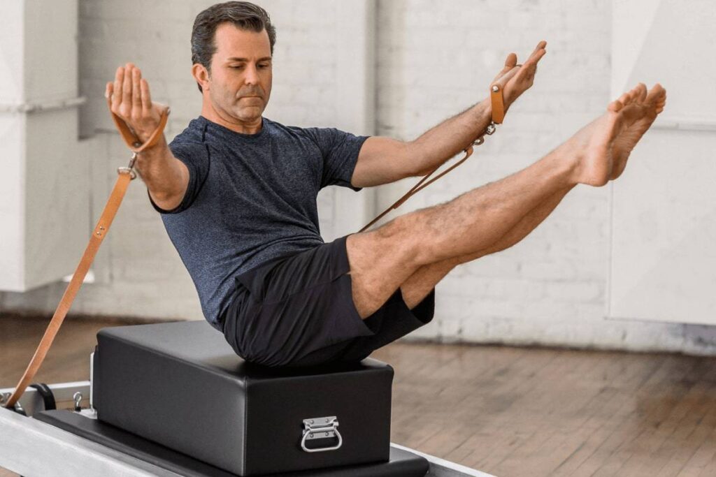 Мужчина выполняет пилатес на коробке Контрологии с ремнями.