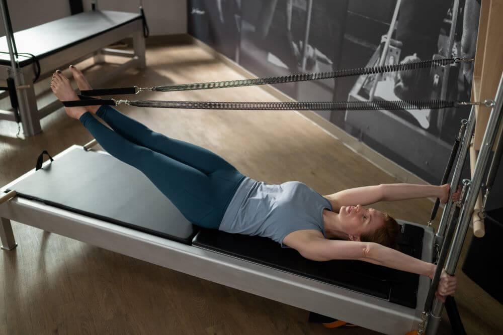 Человек занимается на тренажёре Contrology Reformer с башней и ковриком.