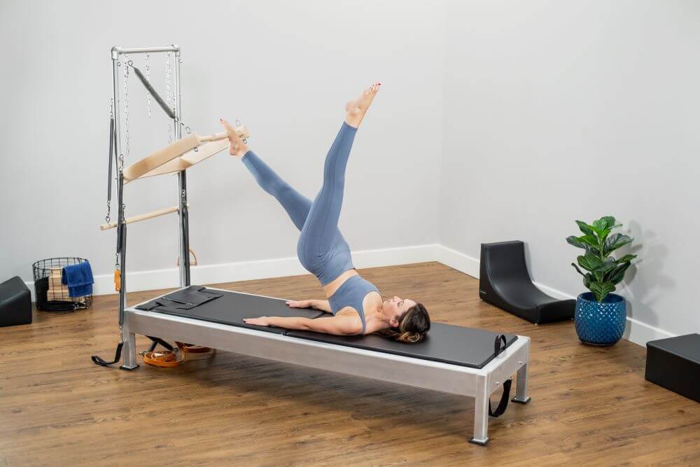 Женщина занимается на тренажёре Contrology Reformer с башней и ковриком.