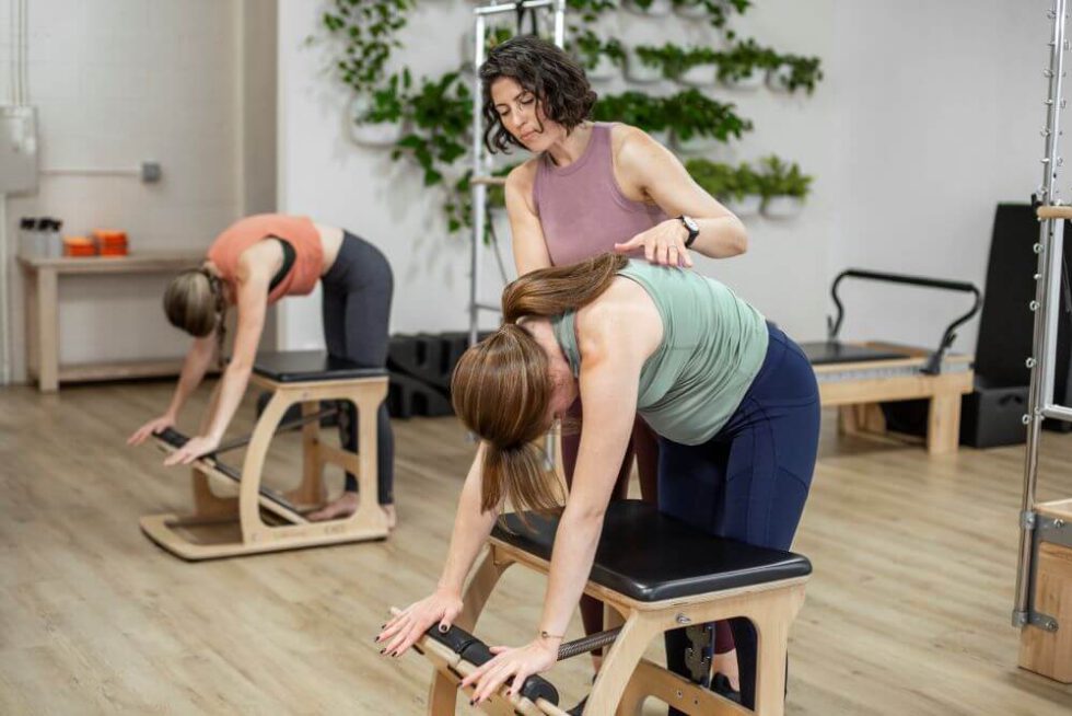 Инструктор помогает студенту на тренажёре EXO Chair во время занятия по пилатесу.