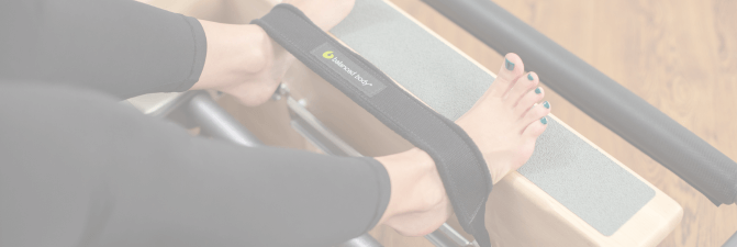 Feet in Balanced Body foot straps on a Pilates reformer.