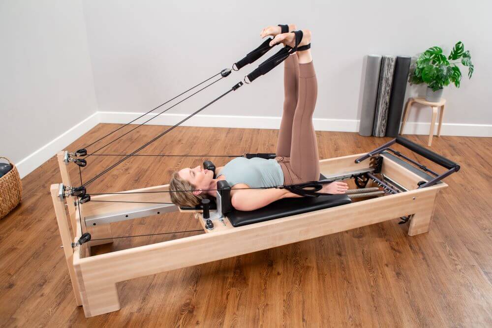 Woman exercising on Studio Reformer Konnector with ropes.