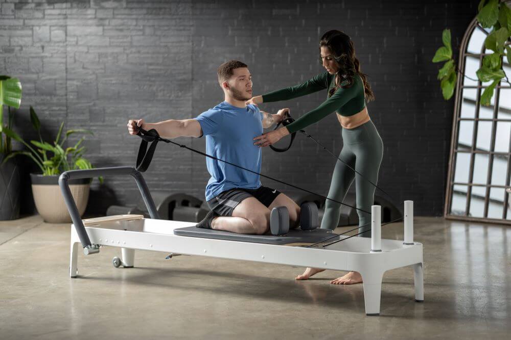Instructor assisting a man on Allegro 2 Reformer in a studio.