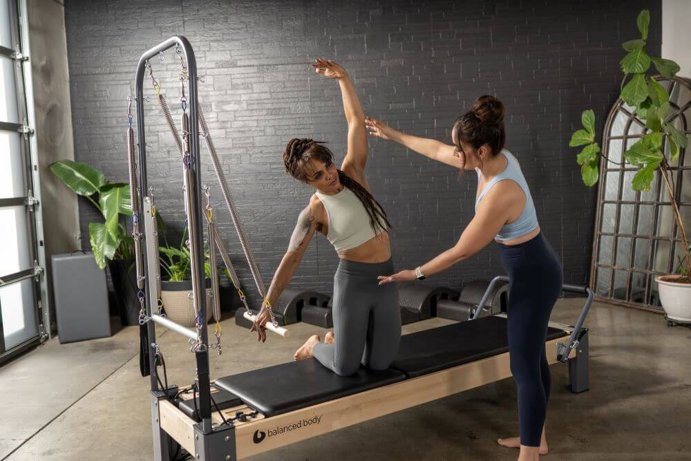 Instructor assists client on Rialto Reformer with Tower in studio.