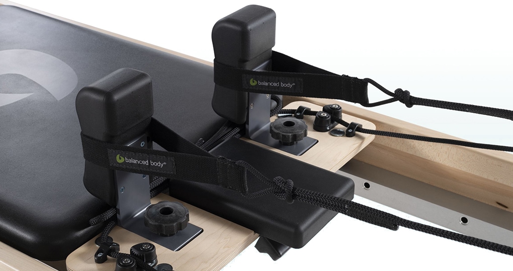 Balanced Body Polska reformer carriage with adjustable ropes and black padded headrest.