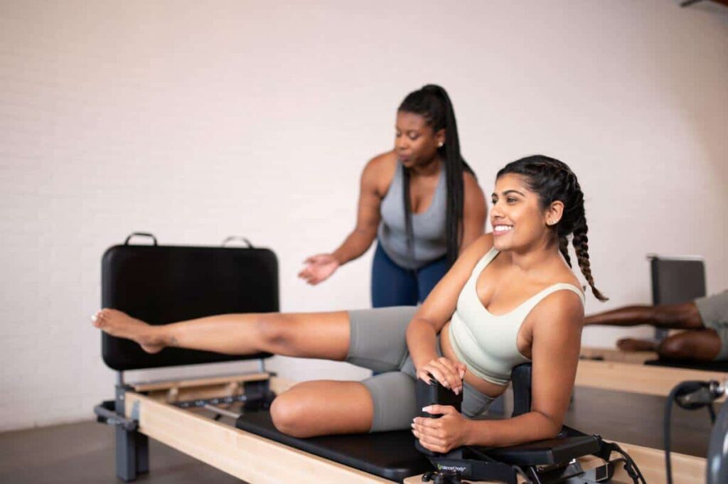 Pilates instruktorė veda mokinį prie Rialto Reformer šuolių lentos