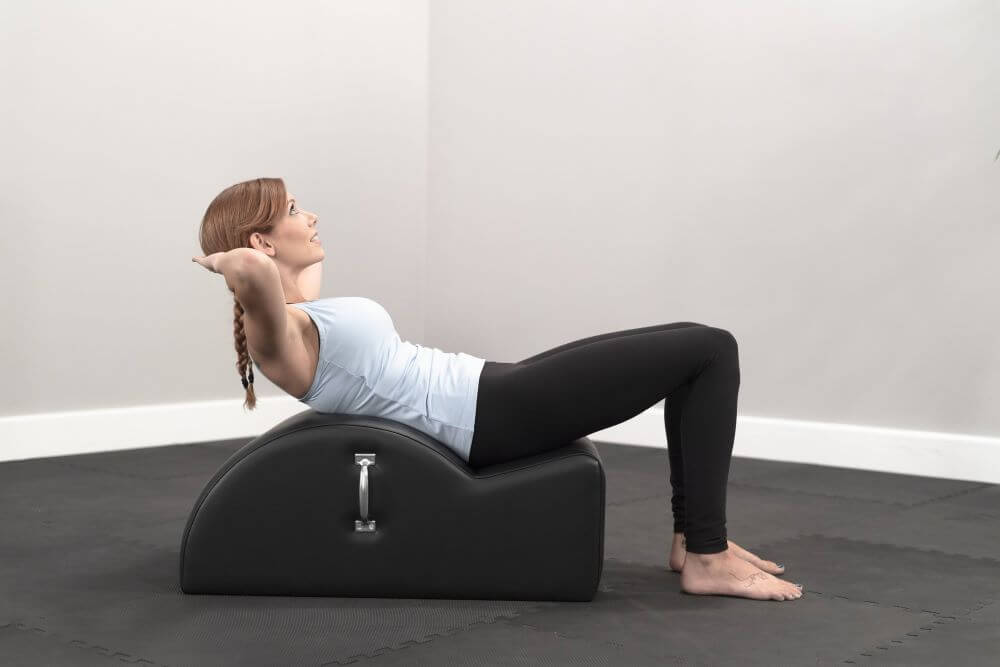 Woman exercising on East Coast Step Barrel in Pilates studio.