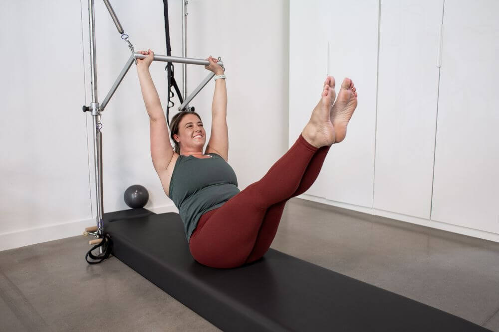 Moteris atlieka pratimą prie sieninės Pilates bokšto įrangos su kilimėlio atrama.