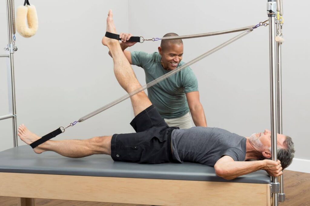 Instruktorius padeda klientui atlikti pilateso pratimą su Trapeze Signature Springs įranga.