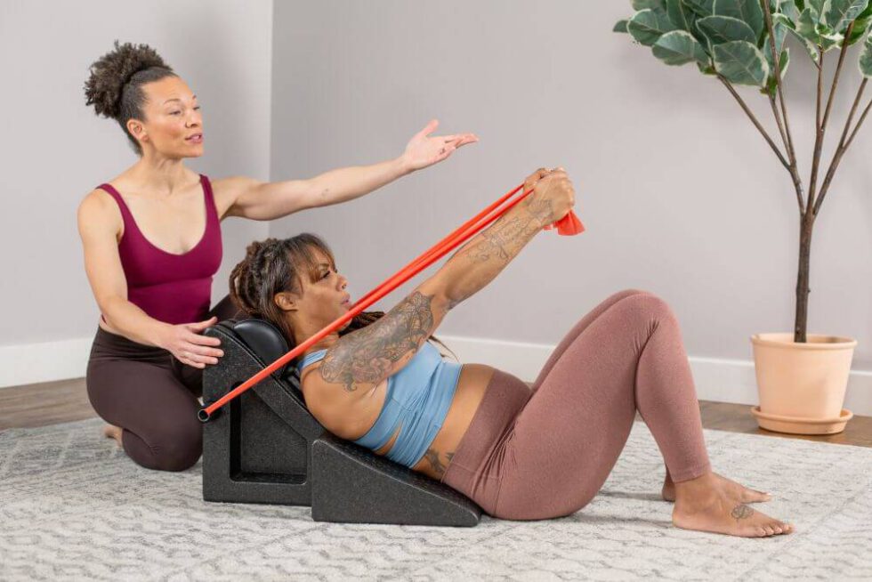 Instructor assisting woman using PilatesAngle with resistance band.