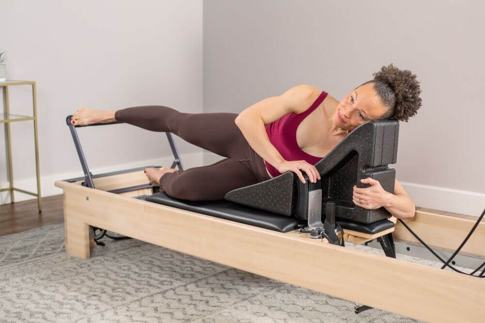 Woman using PilatesAngle on Reformer for side exercise.