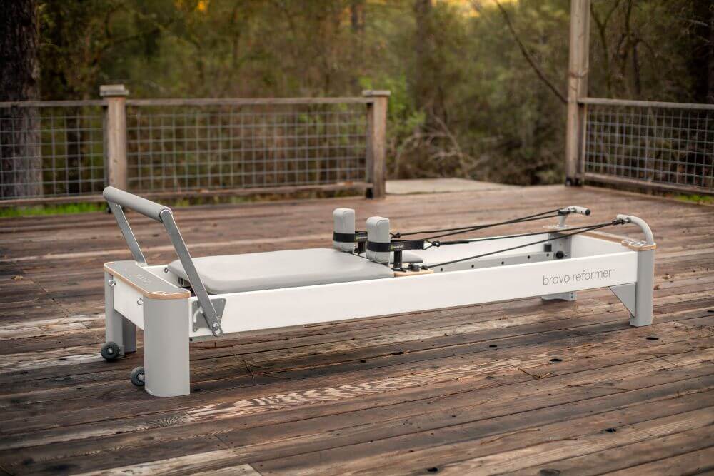 Bravo Reformer Pilates įranga ant medinės terasos, lauko aplinka.