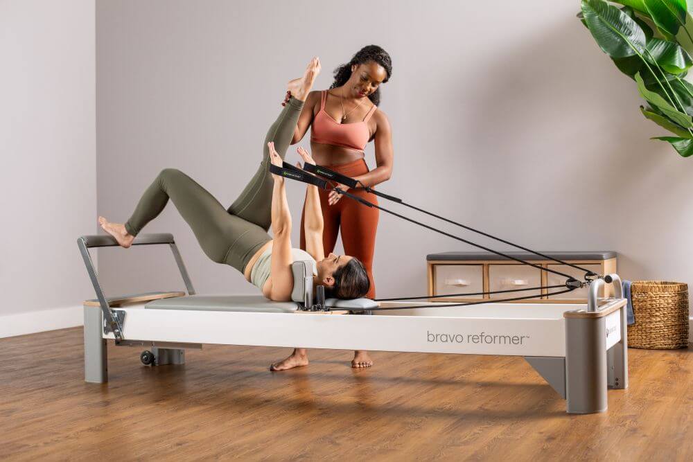 Instruktorius padeda klientui treniruotės metu su Bravo Reformer Pilates treniruokliu.